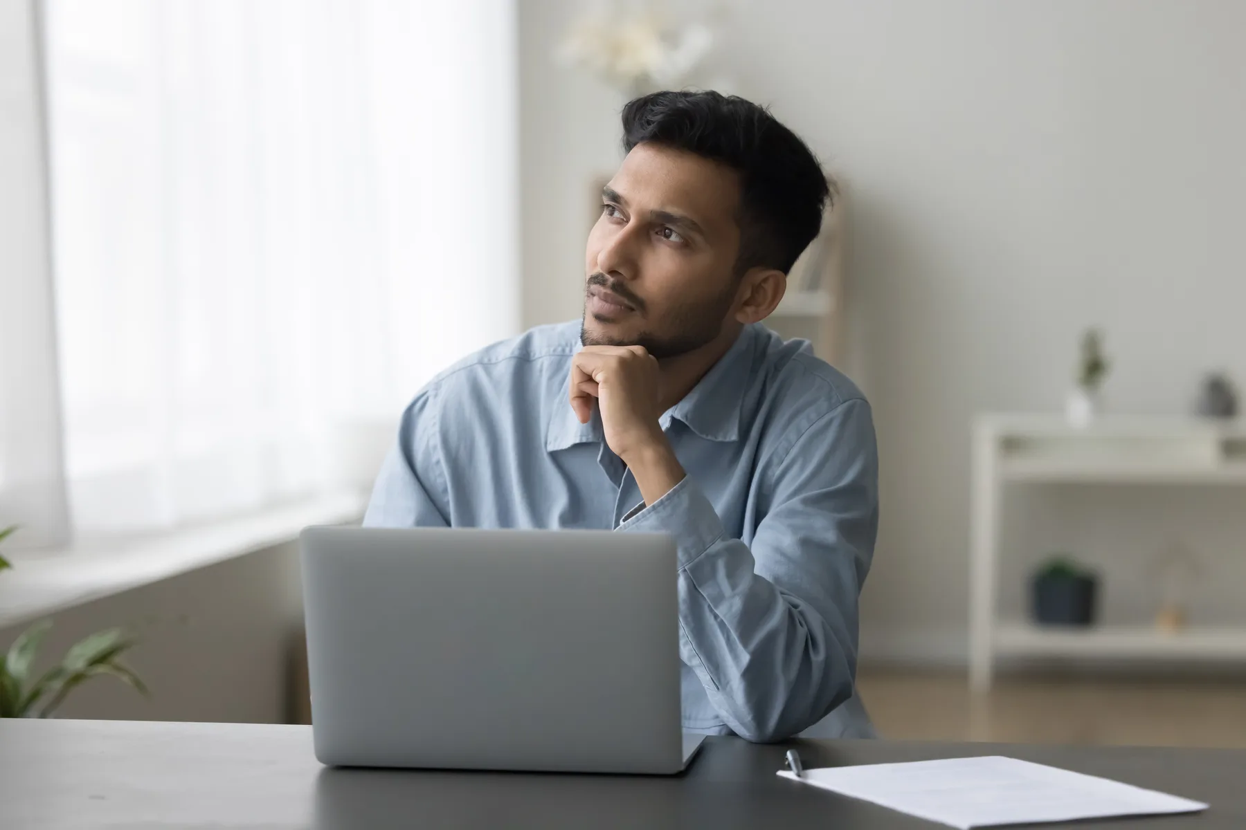 A thoughtful small business professional considering a decision at his laptop in a home office