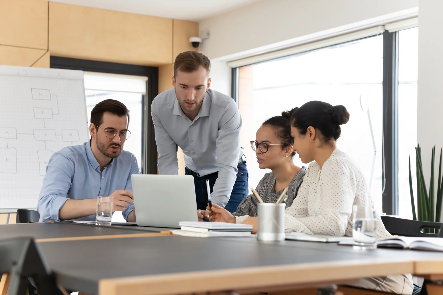 A small business team reviewing a workflow diagram together around a laptop in a meeting room