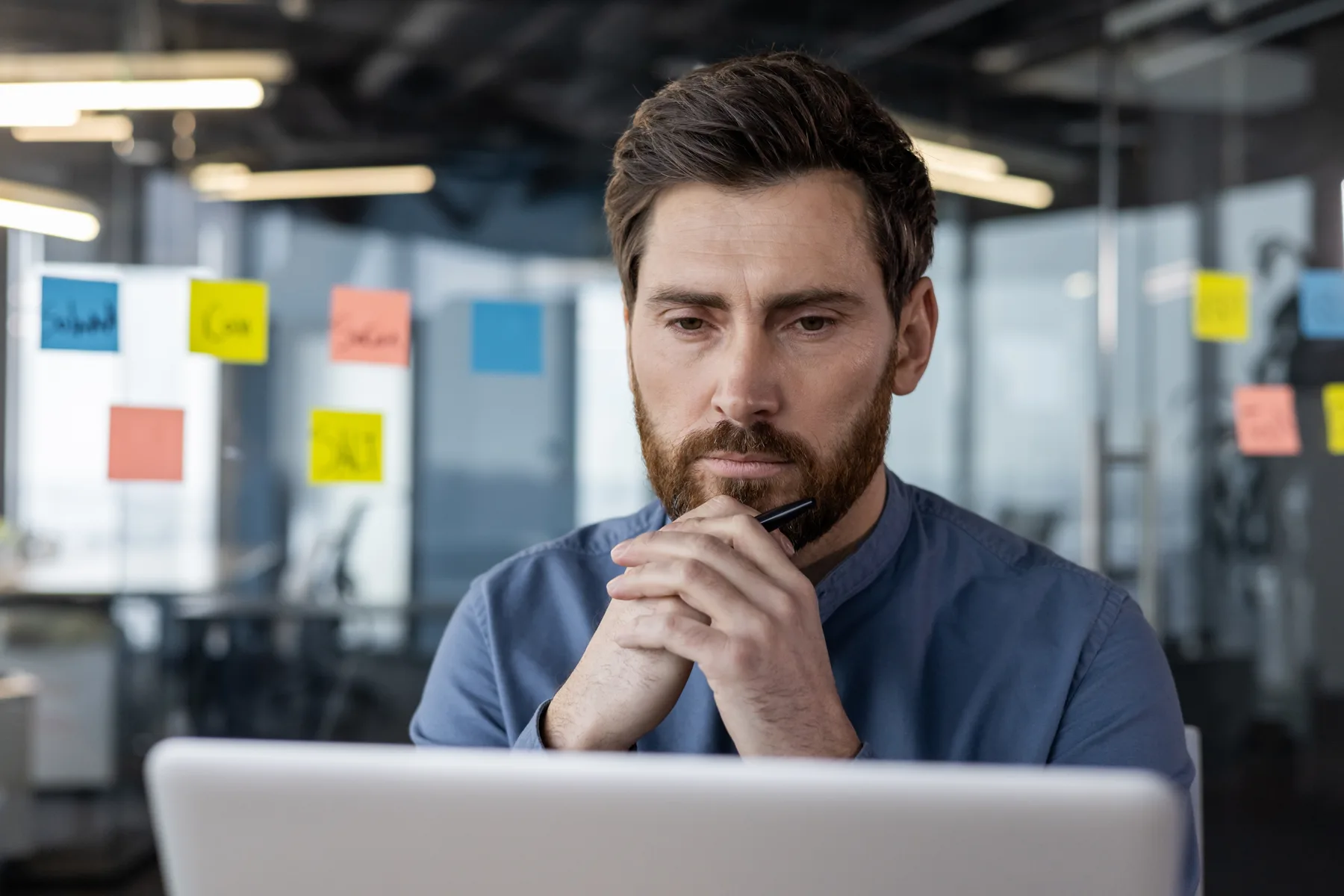 A focused business owner sitting thoughtfully at his laptop in a modern office