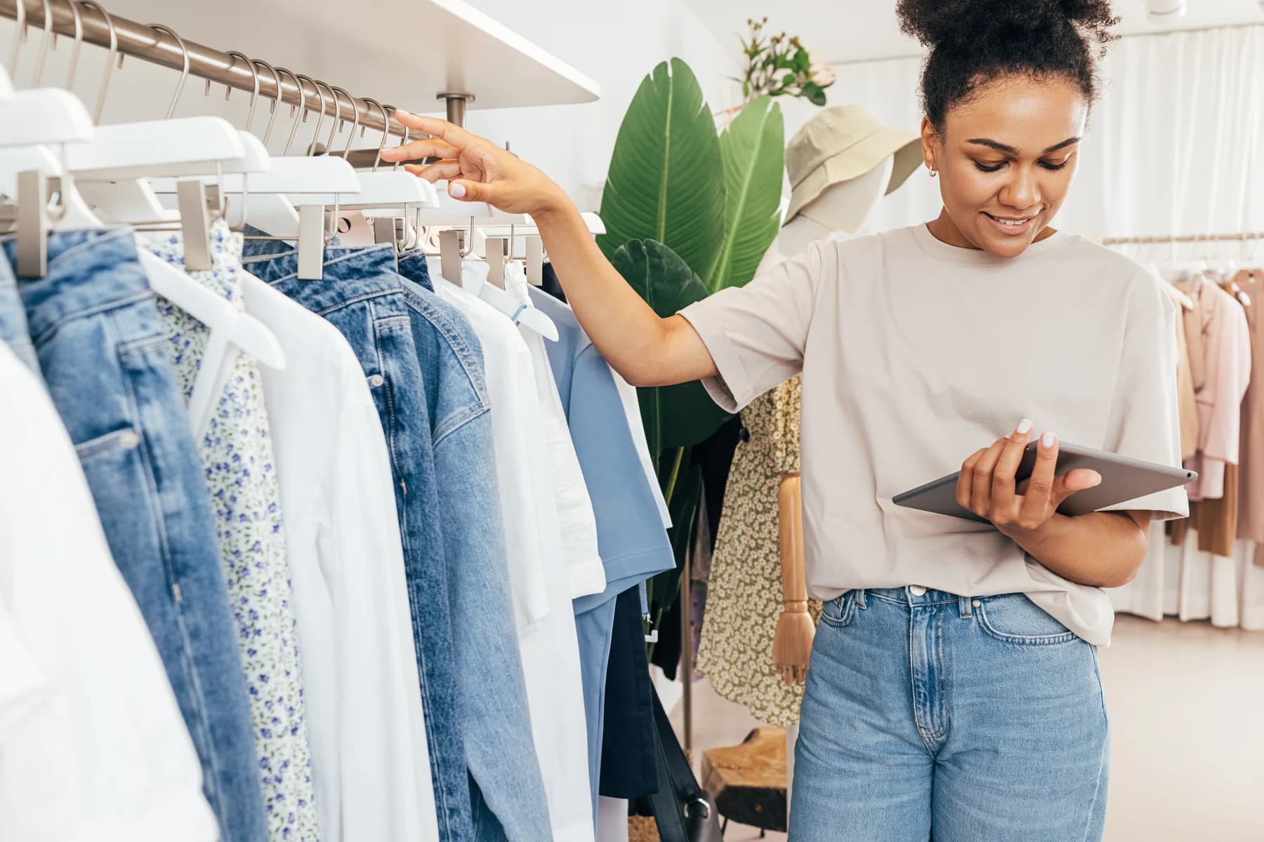 A boutique owner checking inventory on a digital tablet while standing beside a clothing rack