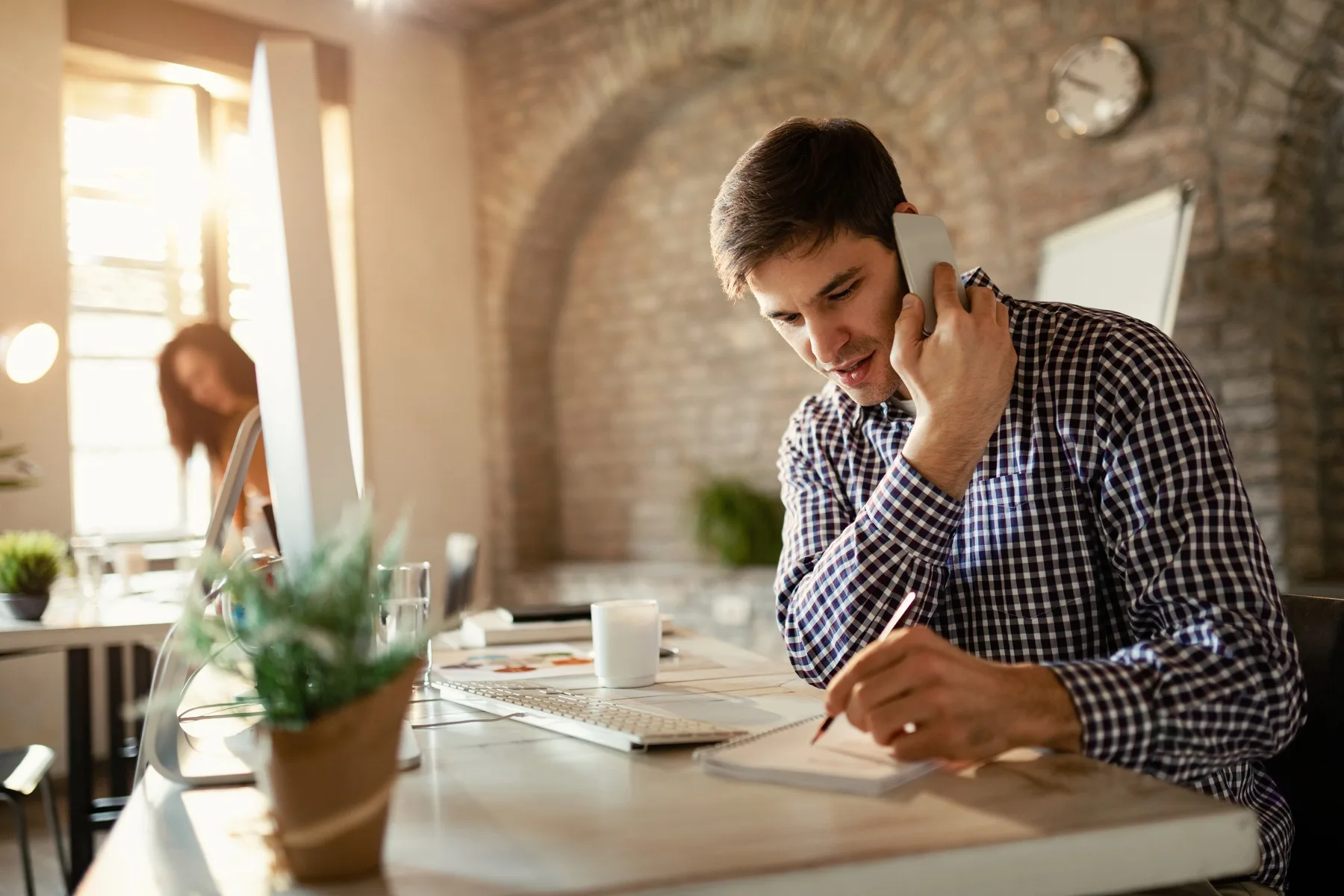 A service business professional taking notes at a desk while talking on the phone with a customer
